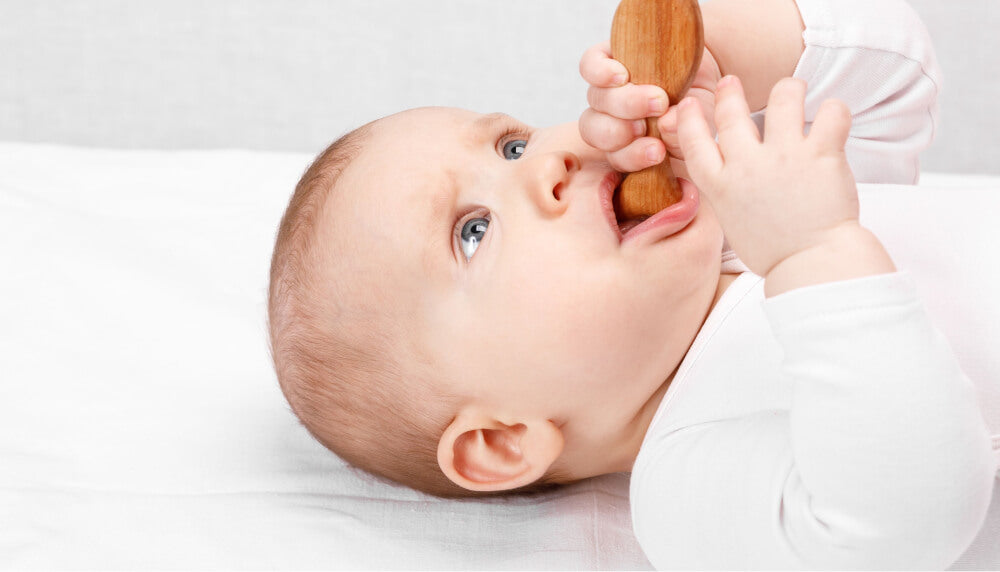 Baby laying in bed while using baby teether.