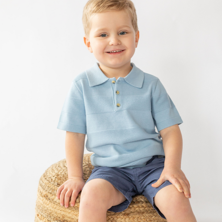 a little boy sitting at the wooden chair wearing Aiden Knit Polo in Cashmere Blue