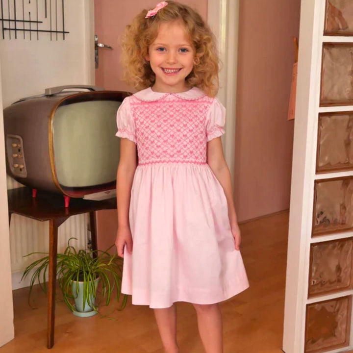 Bow Smocked Dress in Pink a girl standing in front of a TV