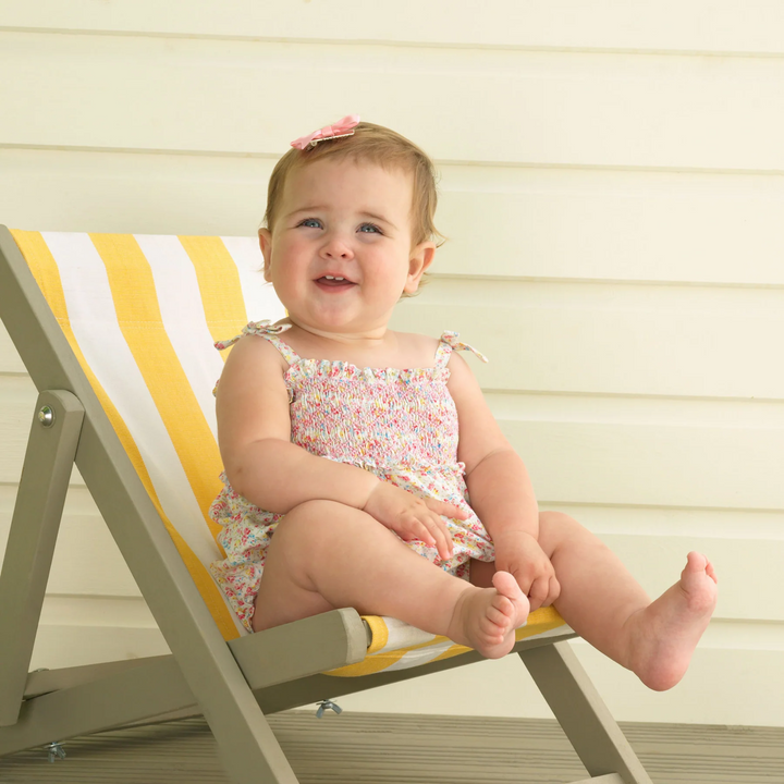 a baby girl sitting at the chair wearing Floral Smocked Bubble