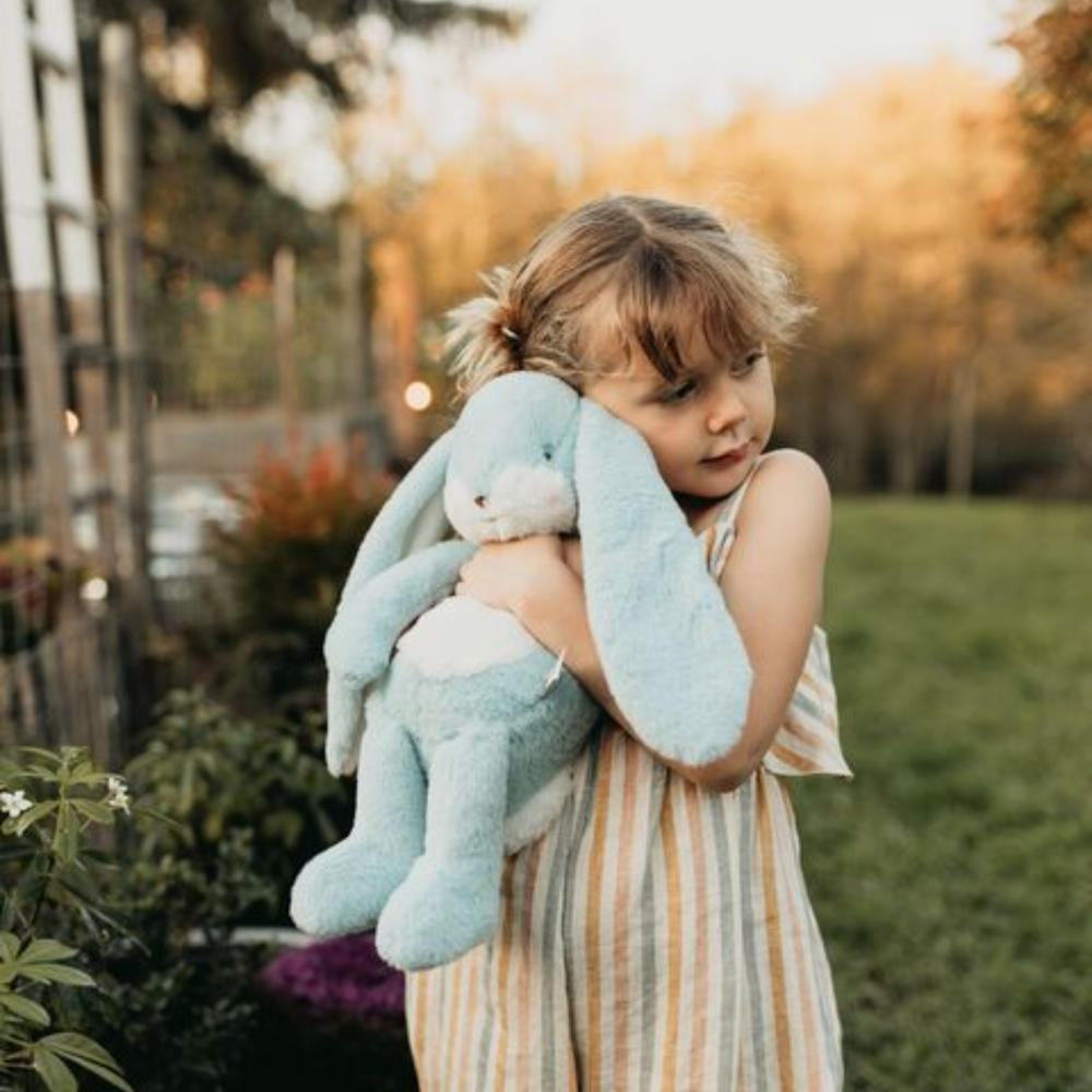 a girl hugging Little Nibble Floppy Bunny in Maui Blue