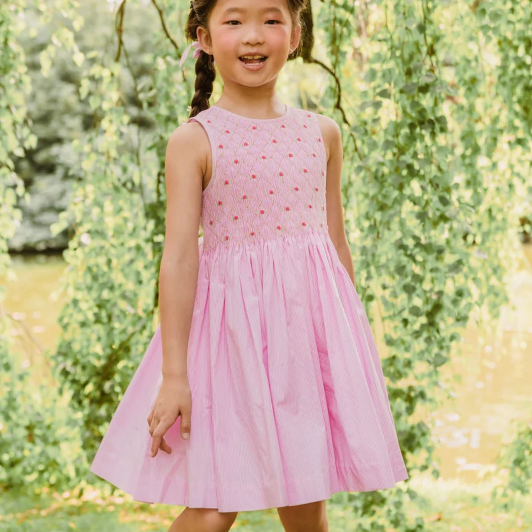 Rose Pink Stripe Sleeveless Handsmocked Dress a gril standing on a bunch of leaves