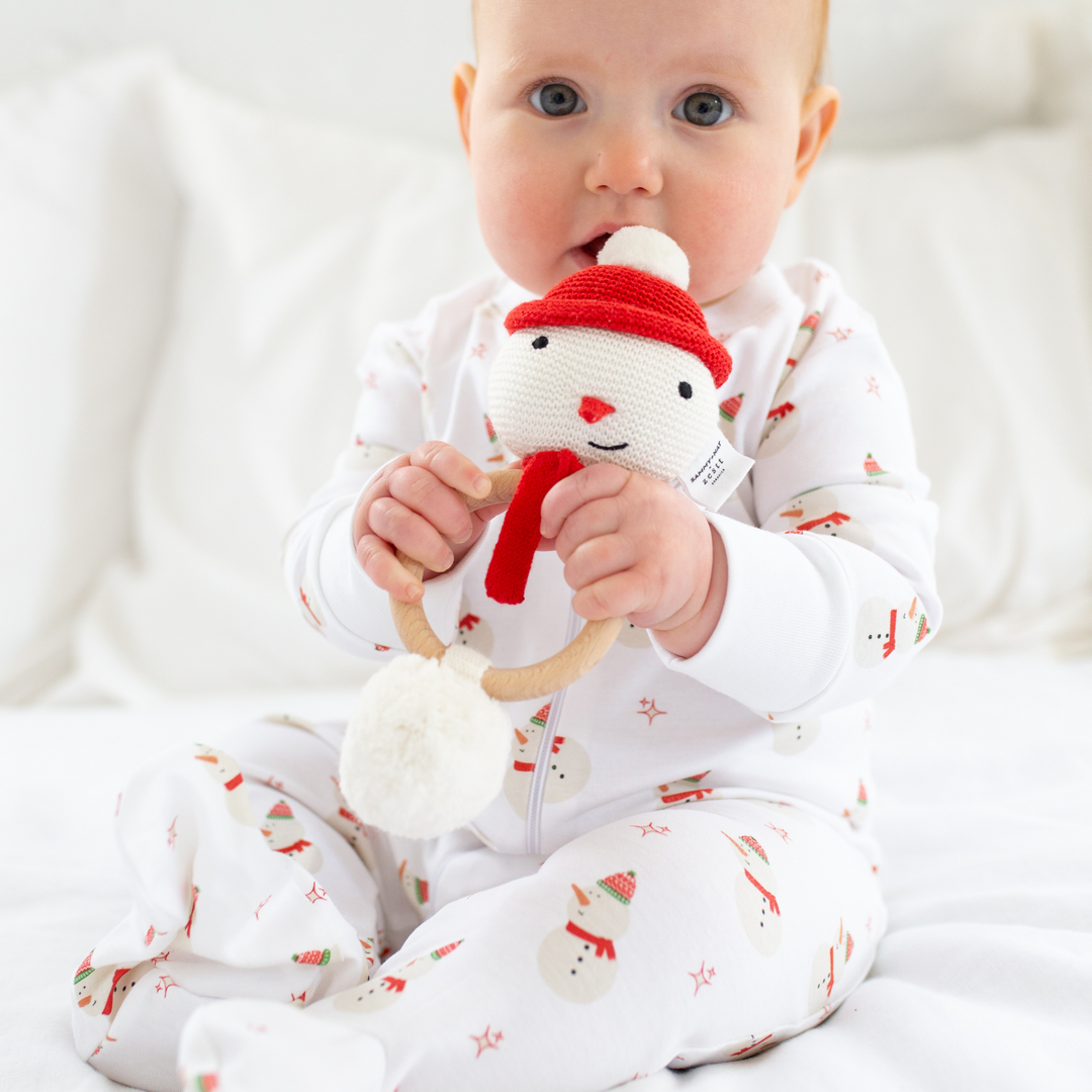 a baby holding the Organic Snowman Rattle in White