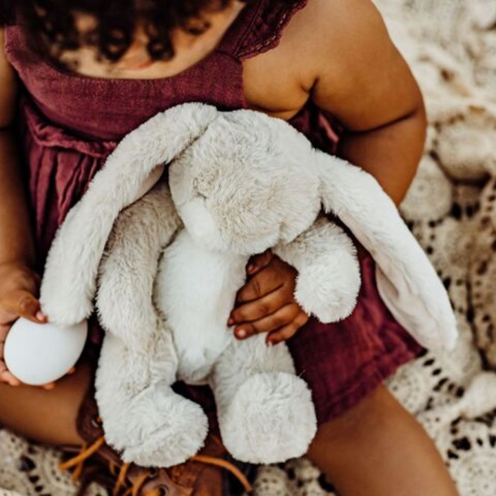 a baby girl holding Wee Nibble Bunny in Cream