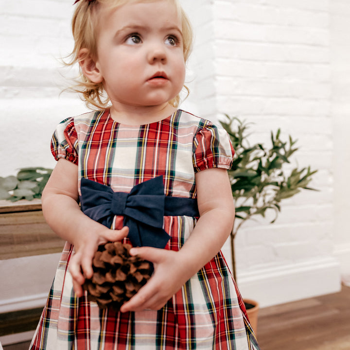 little girl wearing plaid dress holding pine cone